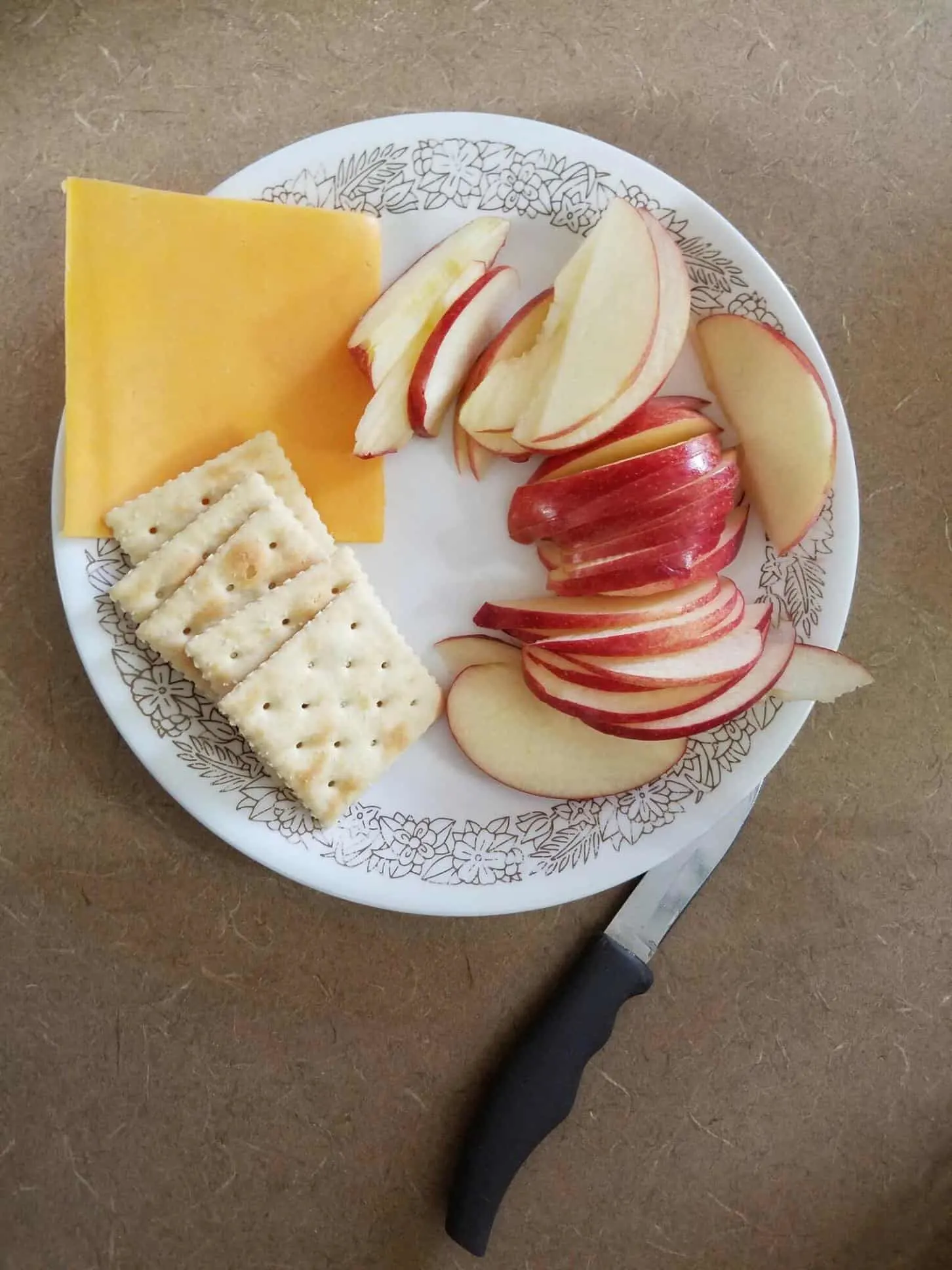 A slice of cheese, crackers, and apples on a plate