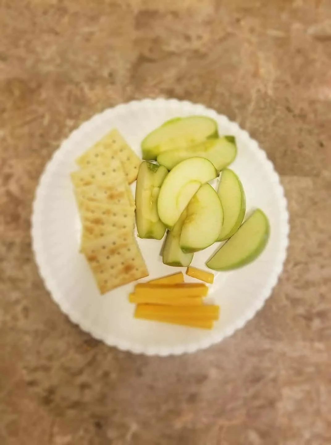 A sliced apple, crackers, and cheese on a plate