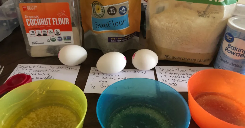close up of bowls, recipes, and ingredients to make 3 variations of keto bread in the microwave. coconut flour, almond flour, and sun flour